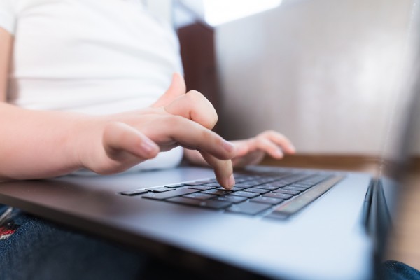 Child's hand typing on laptop keyboard